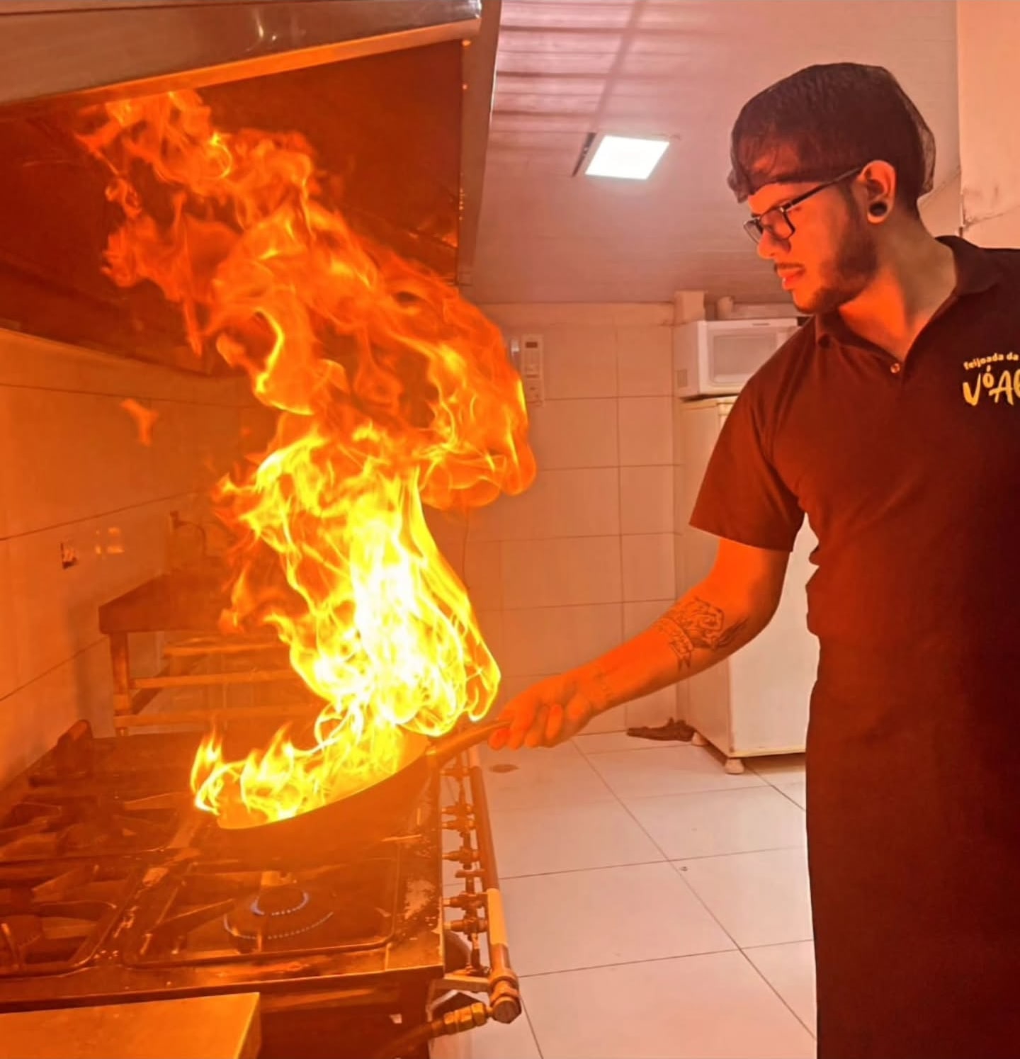 Julio Cabral trabalhando em uma cozinha enquanto uma chama se eleva de uma panela.