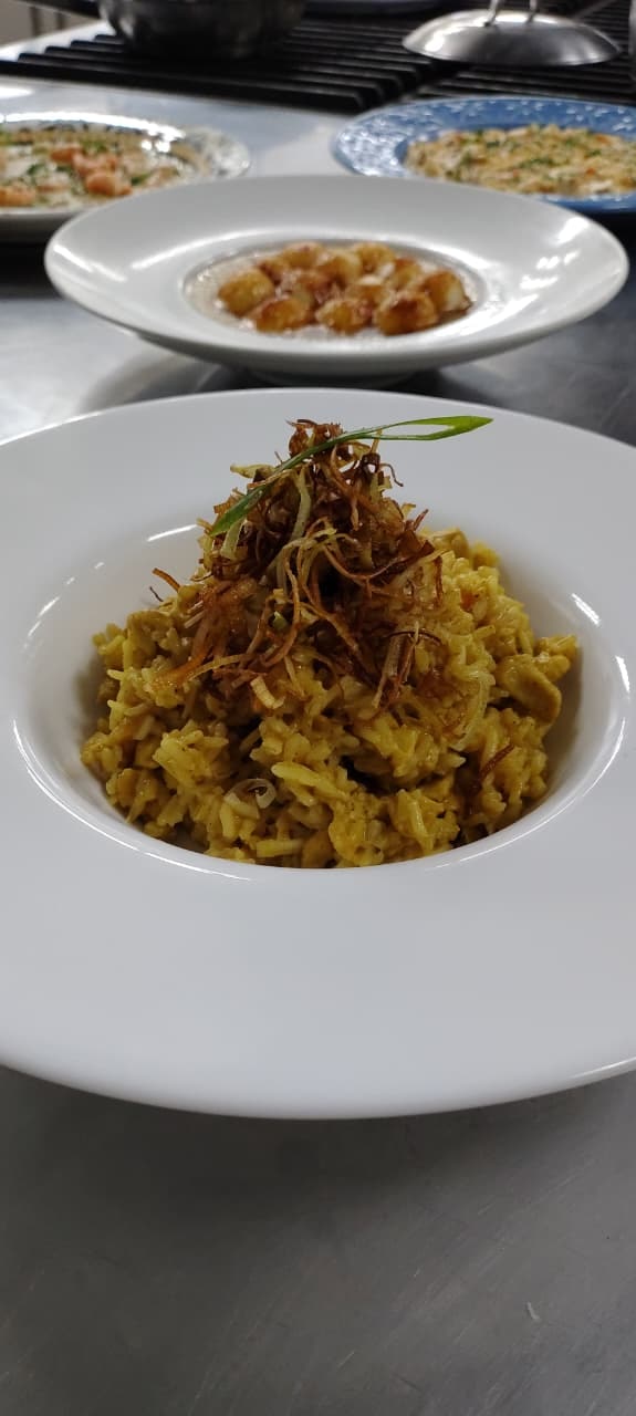 Prato fundo com preparo de arroz finalizado com fios crocantes e folha verde.